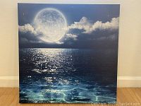 Photo of square canvas wall art leaning against wall, showing night ocean and moon scene.