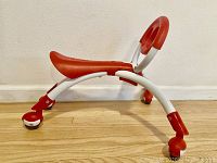 Side view of YBIKE Pewi Walking Buddy showing red and white frame, ergonomic seat and wheels.