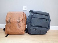 Front view of the tan (Italy) and dark gray (South Korea) backpacks side by side