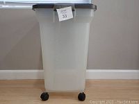 Front view of large translucent plastic storage bin with black lid and wheels showing overall condition.