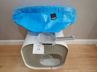 White Modkat top-entry litter box with open front and a blue reusable liner draped over the lid, gray ergonomic litter scoop resting on top. Lot number on paper inside the litter box.