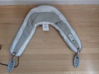 U-shaped Kendal neck and shoulder massager with two handle attachments, gray and white color, laying flat on wooden floor.