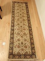 Full view of the traditional patterned rug runner displayed on a wooden floor showing the detailed medallion and floral design with a dark floral border.