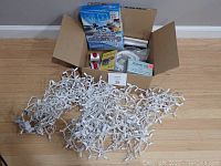 Photo showing white wired Christmas lights laid out with open box of accessories behind