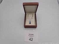 Full set of jewelry in an open brown jewelry box, showing necklace and earrings on cream padding.