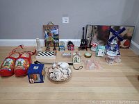Overview of all assorted international souvenir items arranged on floor including painted clogs, shells, ceramics, a checkerboard, and various other souvenirs.