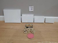 4 different size white painting canvases lined up against wall, wooden alphabet stamps and round pink rubber alphabet stamp pad on floor in front
