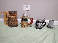 Four antique beer steins displayed on green cloth, showing different materials and lids, including wood and ceramic.