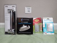 Full set showing SparkPod shower head, shower arm in package, Command adhesive strips, and Velcro picture hanging kit on a green cloth against a beige wall.