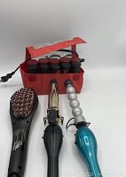 Photo showing black hair straightening brush, black curling iron, blue spiral curling iron, and red pouch with eight curlers