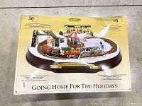 Photo showing the boxed image of the Christmas tabletop train set "Going Home for the Holidays" with a Victorian winter scene and train track.
