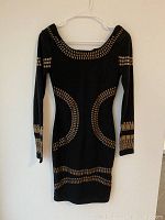 Black long-sleeve dress with tan geometric pattern on neckline, waist, sleeves, and hem, hanging on white hanger.