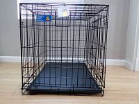 Front view of the black metal folding dog crate with the plastic tray inside, showing the open door space.