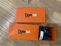 Two orange Tigertail branded boxes, one open showing a dog collar inside.