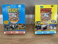 Two sealed boxes of Topps Desert Storm trading cards and stickers, one blue 'Coalition For Peace' edition and one yellow 'Victory Series' edition.