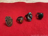 Four vintage men's rings in Western style laid on red background, front view showing designs and stones.