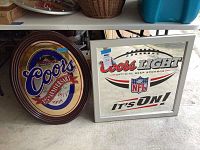 Photo showing both Coors 125th Anniversary oval mirror and Coors Light NFL square mirror side by side on floor.