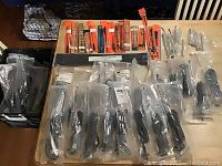 Lot of various antennas in sealed packaging arranged on a table, including black and metallic models in clear bags and branded orange packages.
