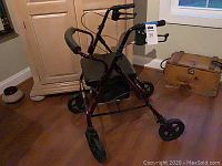 Photo of red Probasics rollator walker with padded seat and backrest, handlebars with hand brakes, and four wheels on hardwood floor in room with furniture.