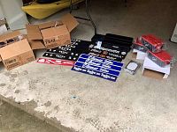 Wide view shot showing items spread on floor: boxes of martini glasses, multiple bar rail rubber mats with various brand logos, organizer trays, and boxed menus.