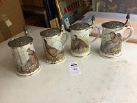Front view of all four porcelain game bird steins with pewter lids positioned on a white surface.