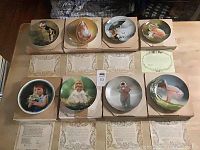 Eight Donald Zolan collector plates in original boxes, arranged on table with certificates of authenticity in front of each plate and noticeable wear on boxes.
