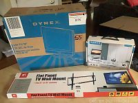 Dynex 19-inch LCD TV box shown with Sanus and HFT TV wall mounts in their original packaging, all boxed and displayed stacked on floor