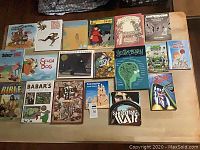 Top-down view of 19 assorted children's books laid out on a table showing front covers and evident wear on some books.