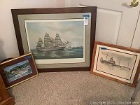 Three framed nautical-themed prints grouped on floor against wall showing sizes and frames