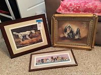 Three framed dog art prints arranged on floor: two prints with dogs in outdoor scenes, one ornate gold frame Shitzu artwork.