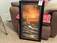 Full view of framed oil painting showing lighthouse scene with waves and sky at sunrise or sunset.
