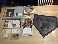 Overall lot layout showing all items on table: framed Clemens item, postage issues, collector plates, patch, door mat