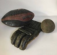 Three vintage sporting goods: Wilson football, leather glove, baseball all showing signs of heavy use and age.