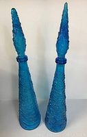 Two tall blue vintage mid-century modern glass decanters displayed side-by-side showing their height and textured pattern.