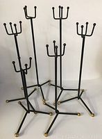 Full view showing all six tall black metal candle holders with tripod bases and gold ball feet, arranged together against a plain white background.