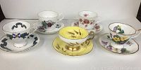 Front view of all five bone china tea cups and saucers with various floral and patterned designs including a prominent yellow cup.