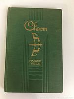 Front cover of the book 'Charm' shows dark green cloth cover with gold embossed title and decorative images.