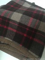 Photo showing brown and red plaid wool blanket folded showing the plaid pattern clearly.