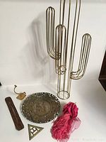 Full lot view showing gold wire cactus sculpture, brass plate, pink tassels, brass triangle, brass hook, and wooden piece.