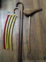 All items laid on wooden floor: two wooden canes, one with curved handle, one seat cane with wooden seat, and four plastic shoe horns (3 yellow, 1 red).
