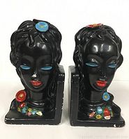 Front view of both chalkware female bust bookends showing the black finish, blue eyelids, red lips, and colorful flowers.