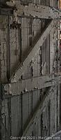 Rear view of vintage solid wood door showing metal strap hinges and diagonal braces with peeling paint and aged wood.