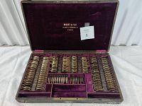Opened case showing rows of brass framed refraction lenses arranged inside a purple velvet-lined wooden box.