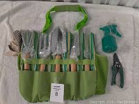 Full set laid out on white towel showing gloves, six gardening tools, spray bottle, pruner, and green striped fabric carrier bag with shoulder strap.