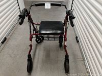 Front view of a maroon walker with cushioned black seat, black wheels, and padded handles.