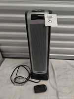 Front view of the tall, slim Lasko air heater with metal mesh grille and remote control placed in front.