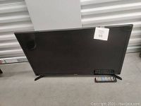 Front view of Samsung 32 inch smart TV with two remotes in front on the floor.