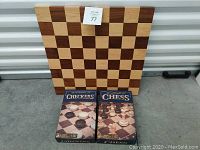 Wooden checker and chess board standing upright behind boxed sets of checkers and chess pieces on the ground.
