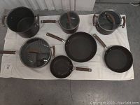 Top view of the 7 piece cookware set laid out on a white cloth showing all pots and pans with brown handles and black interiors.