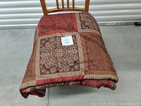 Queen size bed cover folded and placed on wooden chair, showing the patchwork pattern with red and brown floral and geometric squares.